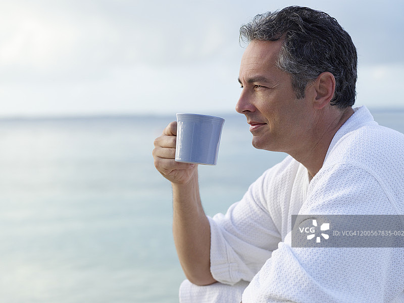 穿着浴袍的男人在海边喝咖啡图片素材