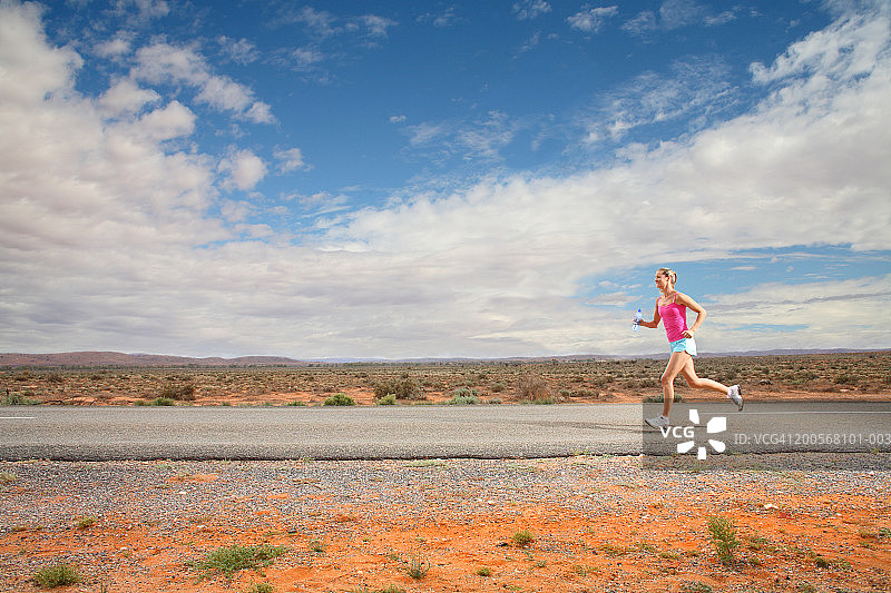 在沙漠公路上跑步的女人，侧视图图片素材