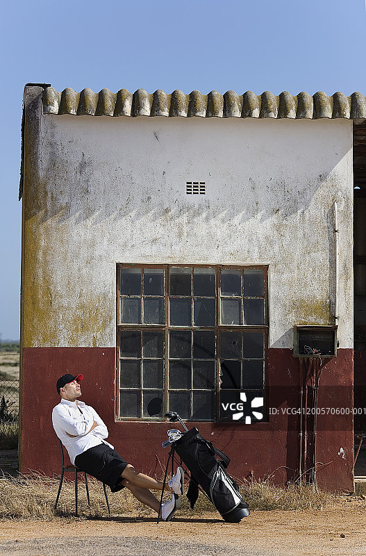 男人坐在建筑物外，手边放着高尔夫球杆图片素材