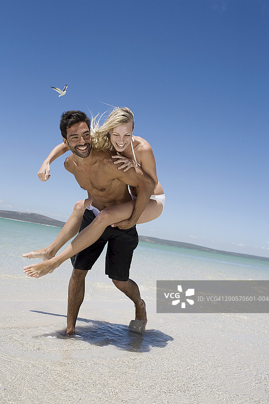 年轻男人在海滩上背着年轻女人，面带微笑图片素材