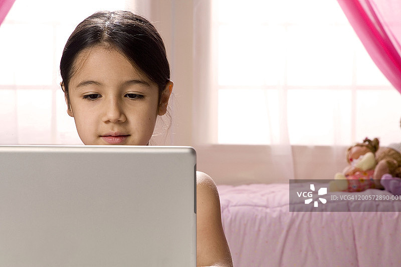 在卧室里使用笔记本电脑的6-7岁女孩图片素材