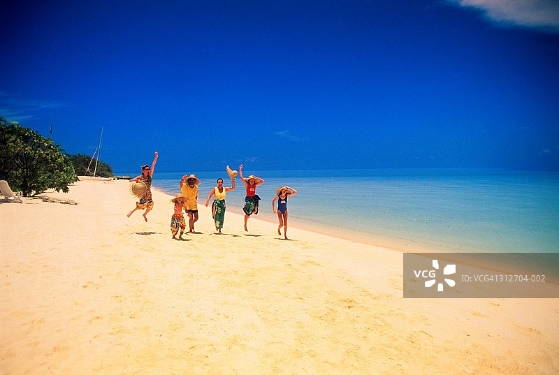 在马尔代夫热带海滩上奔跑的穿着沙滩装的家庭图片素材