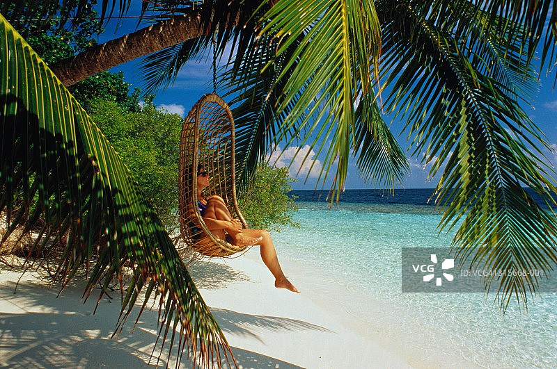 马尔代夫伊胡鲁岛：女子坐在悬挂于海滩棕榈树上的藤椅上图片素材