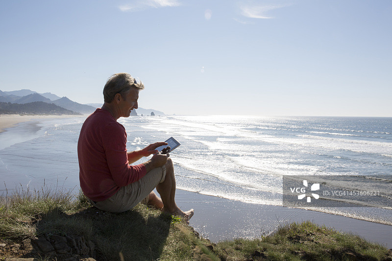 男人在海滩上方的悬崖上使用数位板图片素材