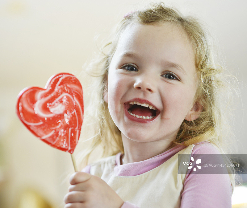 女孩笑着拿着心形棒棒糖图片素材