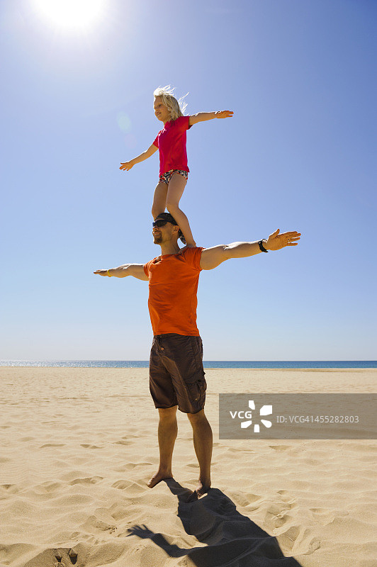 女孩站在父亲的肩膀上，在海滩上图片素材