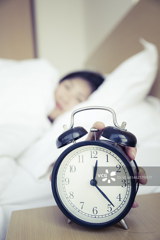 困倦的女人在床上伸手去拿闹钟图片素材