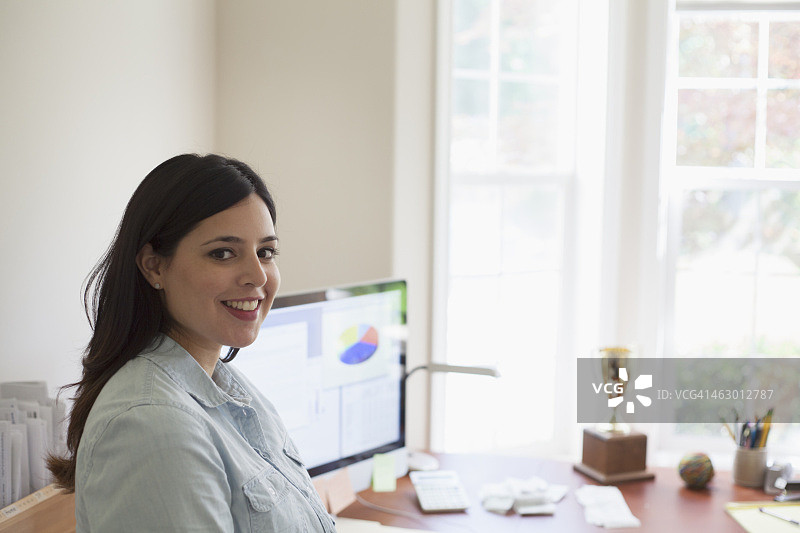 在办公桌旁微笑的西班牙裔女商人图片素材