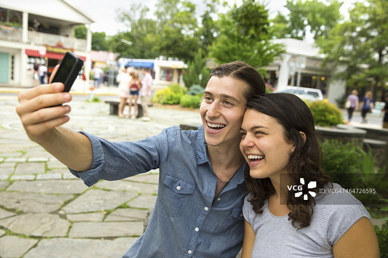 一对年轻情侣肩并肩地拍照和嬉戏。图片素材