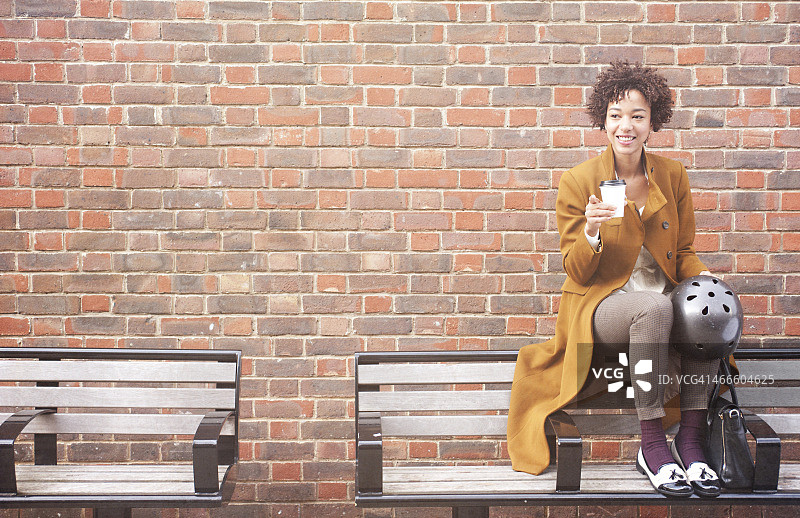 在砖墙边的长椅上等待的微笑女人图片素材