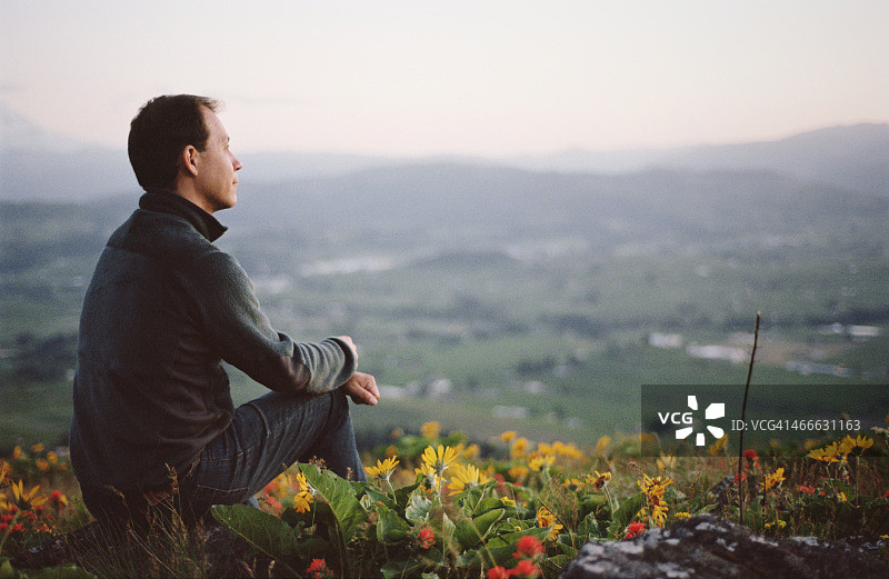 男人坐在山坡上，周围是野花图片素材