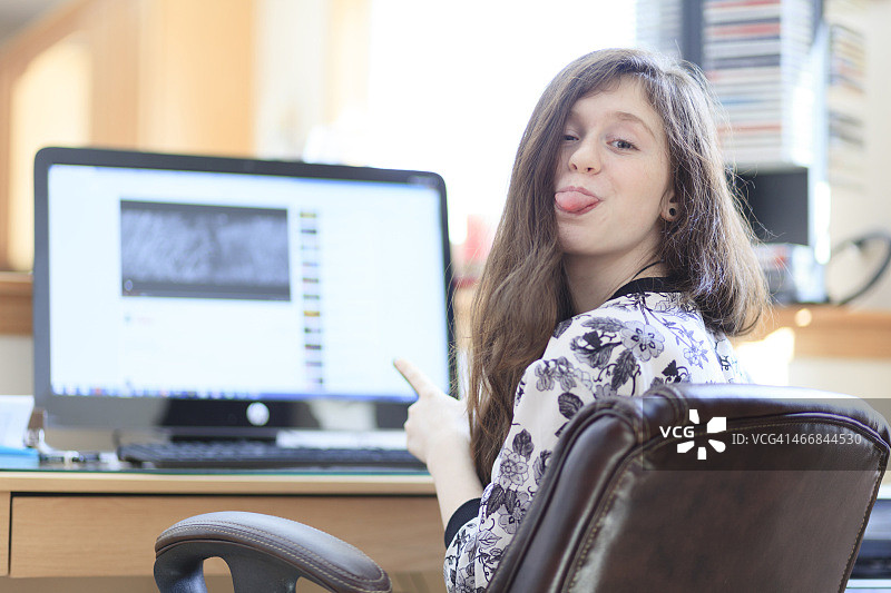 在电脑前用手机发短信聊天的少女图片素材