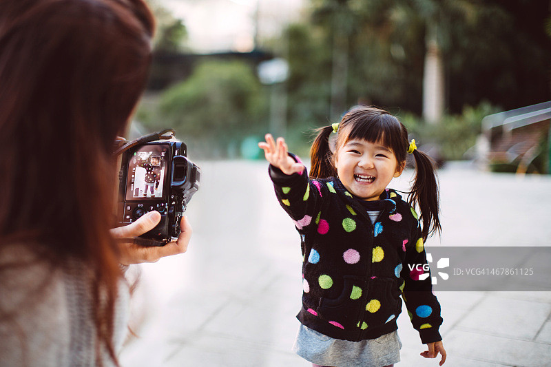 妈妈在公园为蹒跚学步的女孩拍照图片素材