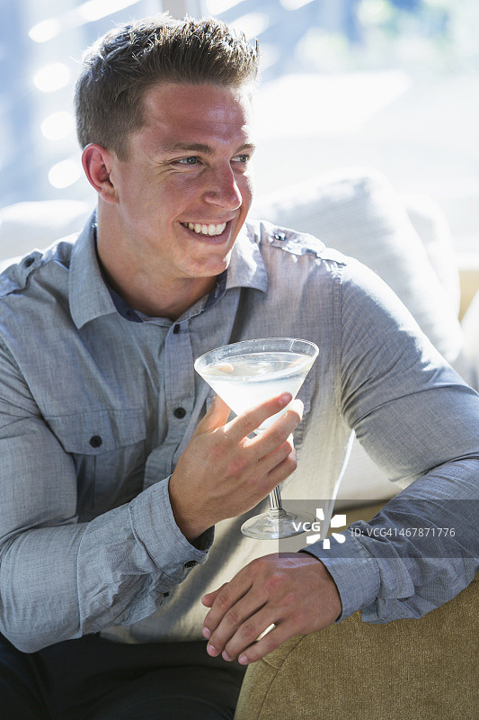 年轻男人手持马提尼酒坐在沙发上图片素材