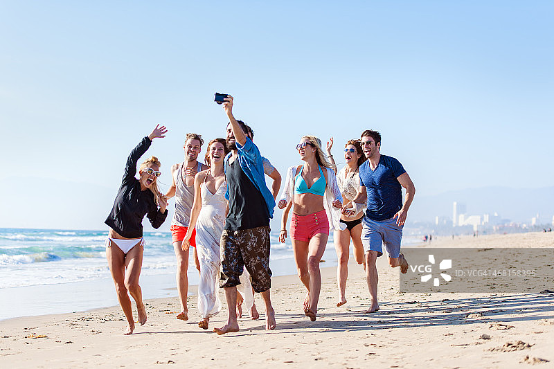 一群朋友在海滩上奔跑和拍摄图片素材