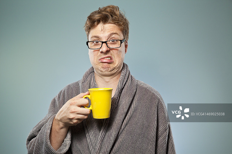 穿着长袍的男人用黄色马克杯喝着劣质咖啡图片素材