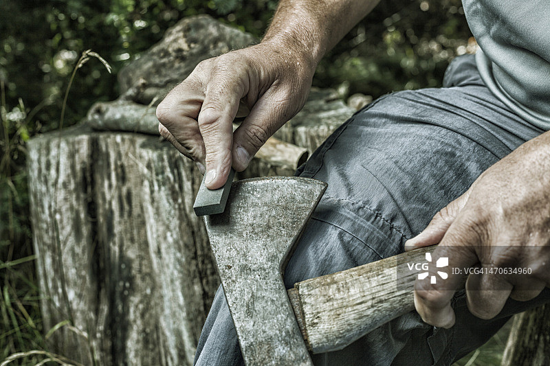 成年男子用磨刀石磨锈迹斑斑的斧头图片素材