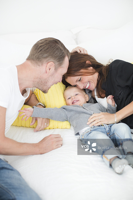 幸福的父母在床上和儿子玩耍图片素材