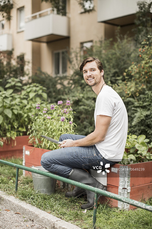 带着园艺设备的年轻男子坐在花园里全身像图片素材