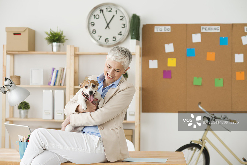 快乐的中年妇女带着她的宠物在办公室图片素材