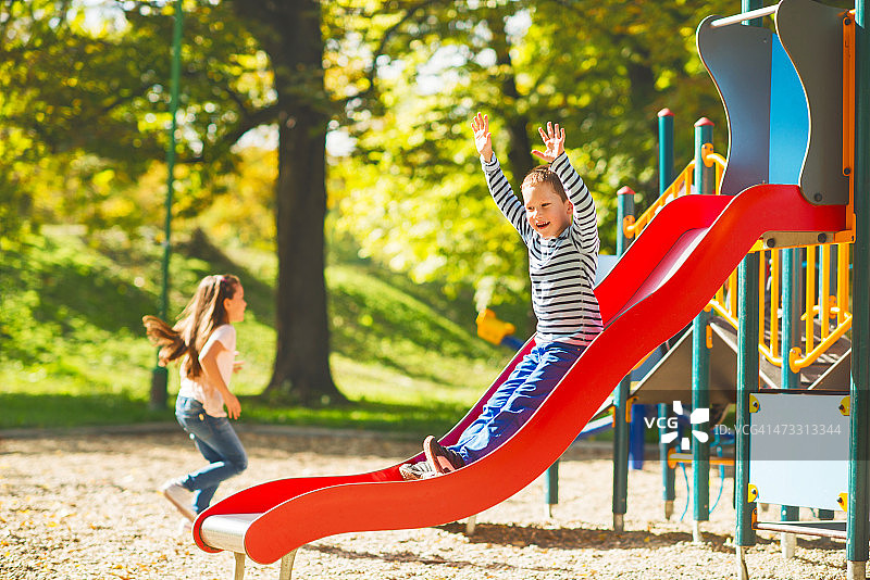 快乐的小男孩在户外滑滑梯，举起双臂。图片素材