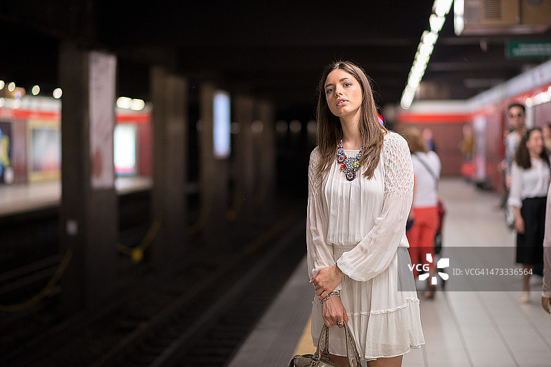 穿着白色连衣裙等待地铁的年轻漂亮女人图片素材