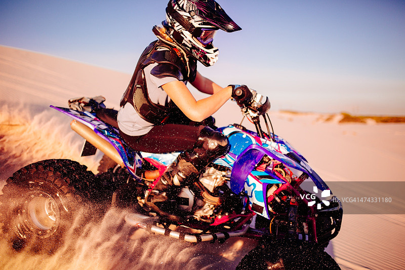 女孩戴着防护装备在沙丘上驾驶四轮赛车图片素材