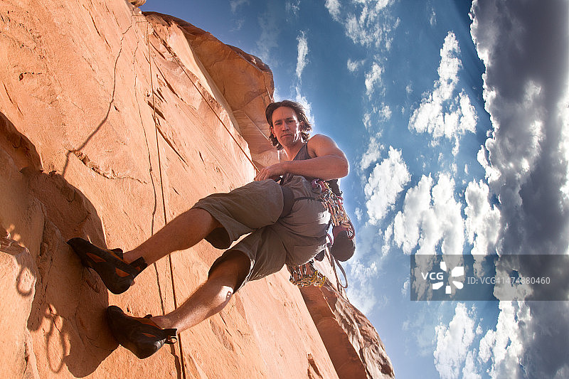 在云景下攀登砂岩悬崖的年轻男子图片素材