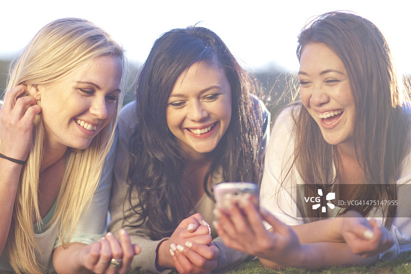 三个年轻女人在公园里看手机图片素材