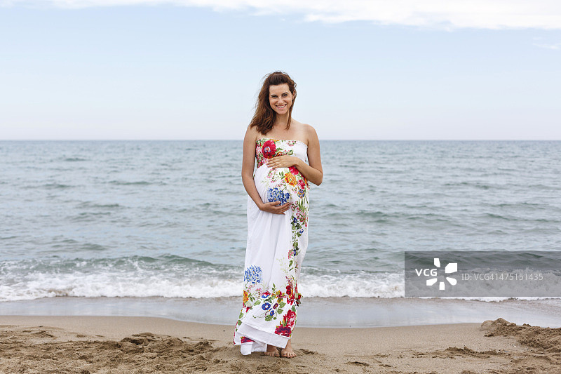 站在海滩上，手扶着肚子的孕妇图片素材