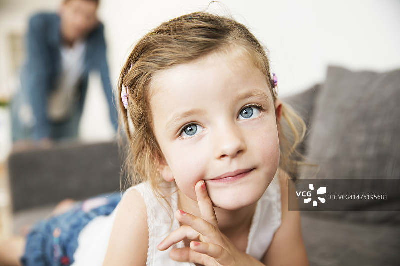 小女孩躺在沙发上，父亲站在背景中的肖像照图片素材