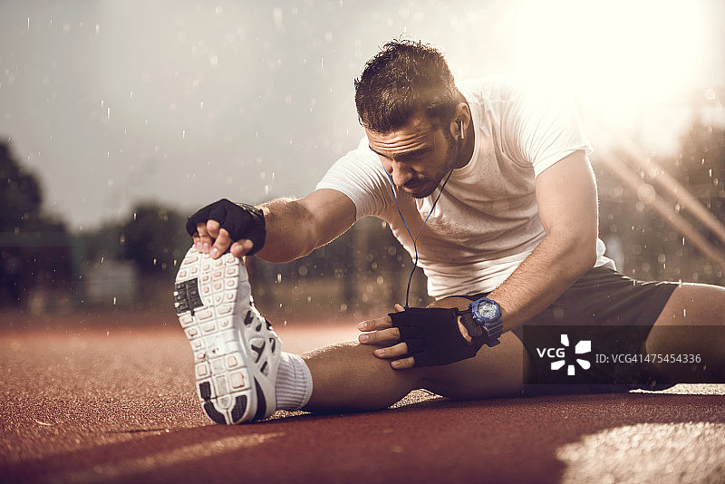 在雨中伸展腿的年轻男人图片素材