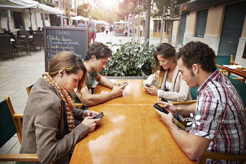 四个朋友在咖啡馆里看手机图片素材