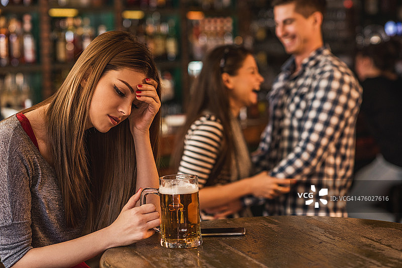 酒吧里悲伤的年轻女人，背景是一对快乐的情侣图片素材