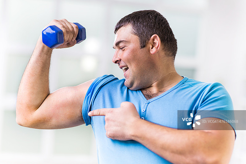 胖男人展示他的肱二头肌，同时拿着一个哑铃图片素材