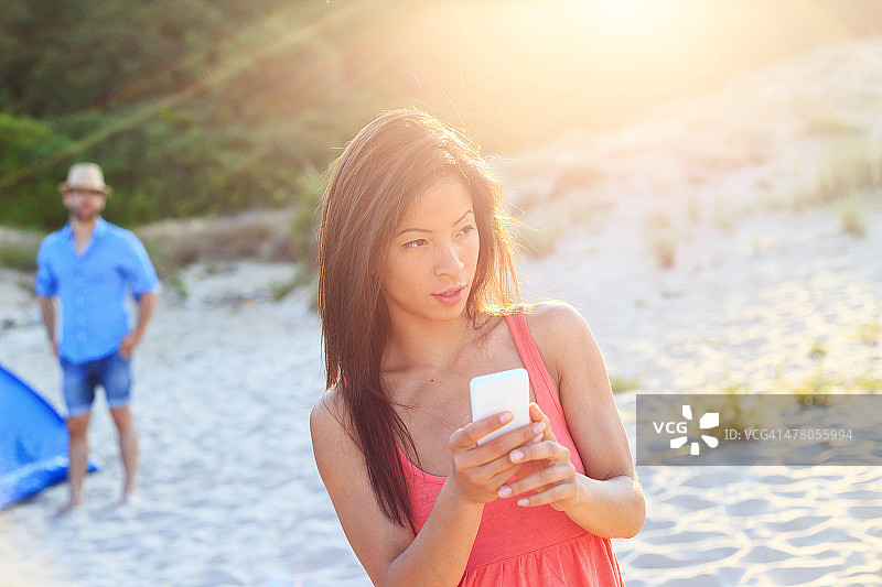 在海滩上使用手机的亚洲女孩图片素材