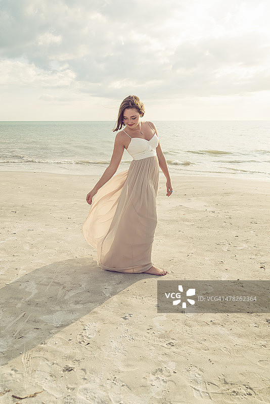 在海滩上穿着舞会礼服的年轻女人图片素材
