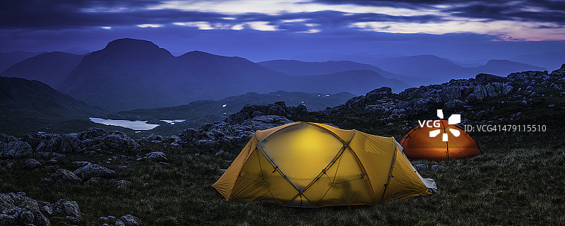 山区荒野营地黄昏全景中被照亮的彩色帐篷图片素材