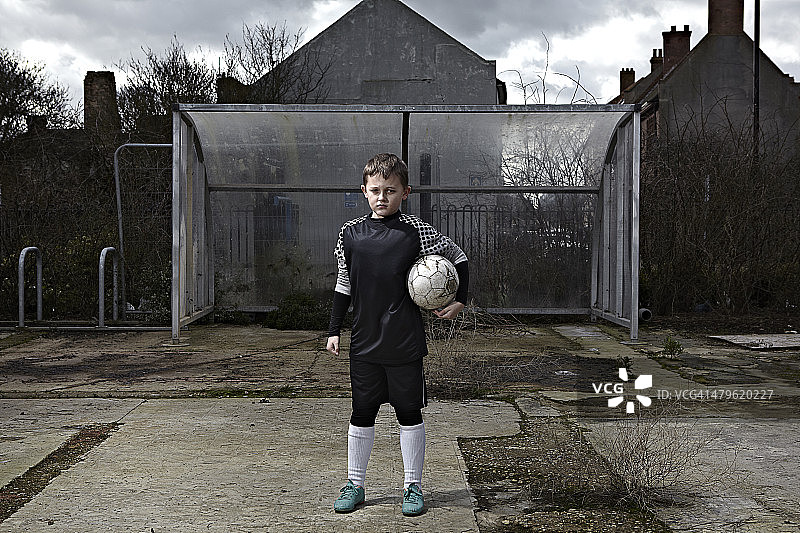 儿童站在那里，一只胳膊下抱着一个足球图片素材