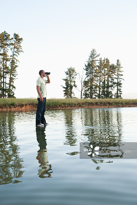 男子站在水中用双筒望远镜观察图片素材