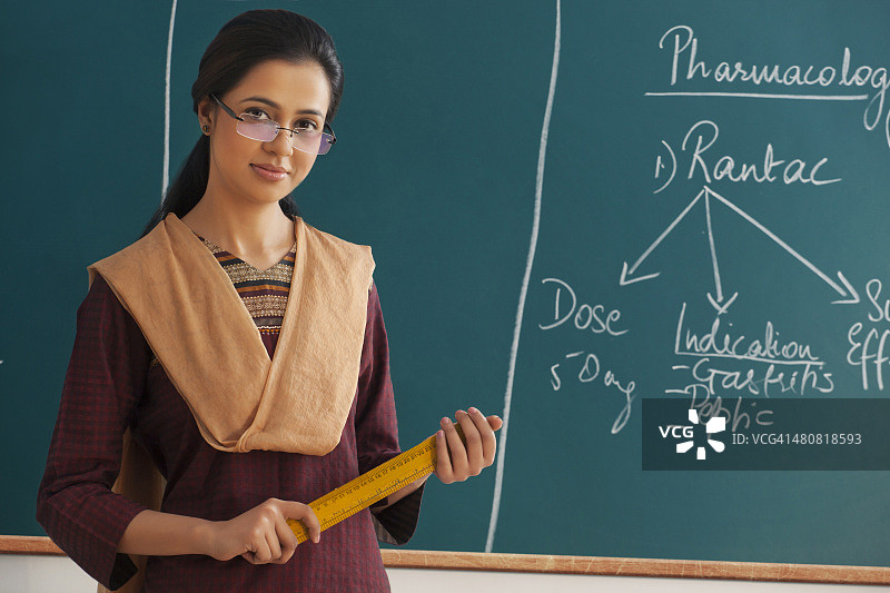 拿着尺子靠在黑板上的年轻女教师肖像图片素材