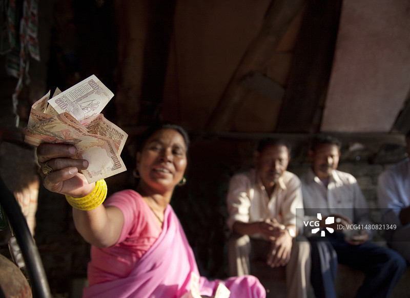 女商贩在摊位拿着印度货币，顾客坐在背景中图片素材