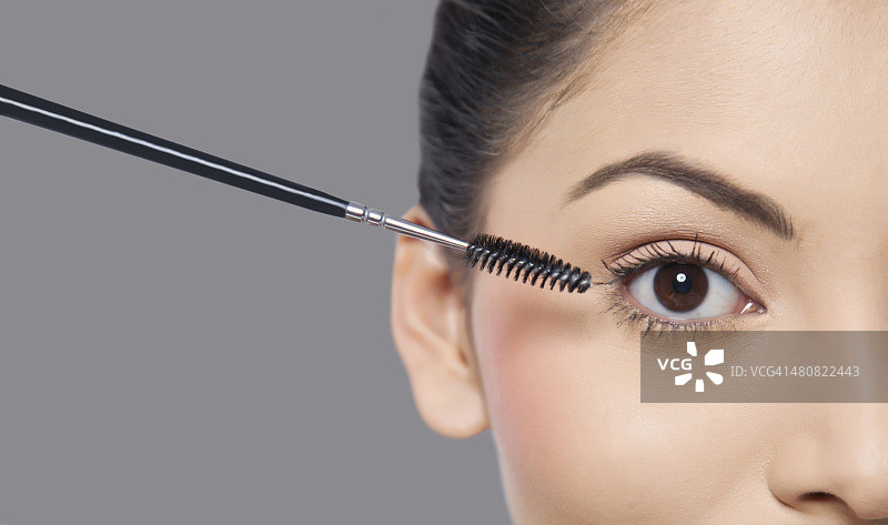 在灰色背景下，年轻女子涂睫毛膏的裁剪图像图片素材