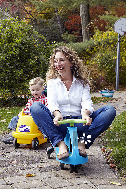 母亲和年幼的儿子在花园里骑玩具车图片素材