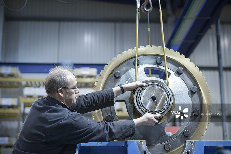 工程师使用起重机在工程工厂移动大型齿轮图片素材