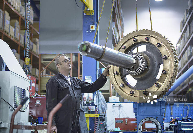 工程师使用起重机在工程工厂移动大型齿轮图片素材