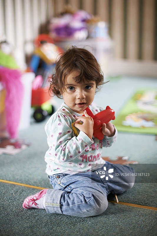 女童坐在游戏室地板上玩红色玩具图片素材