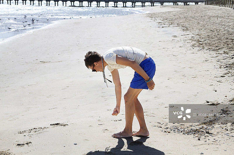 年轻男人在澳大利亚墨尔本港海滩上寻找贝壳图片素材