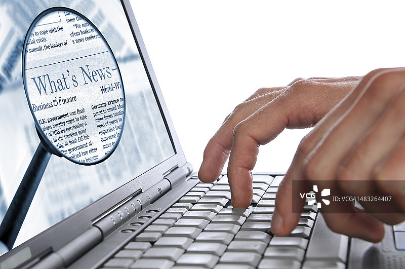 在线新闻，男人的手在笔记本电脑键盘上，屏幕上有放大镜图片素材