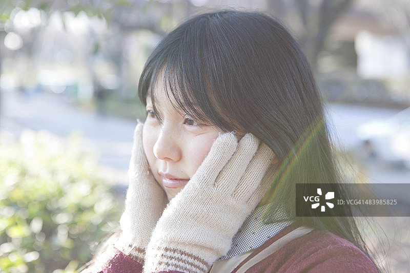 戴着冬季手套触摸脸颊的女学生图片素材